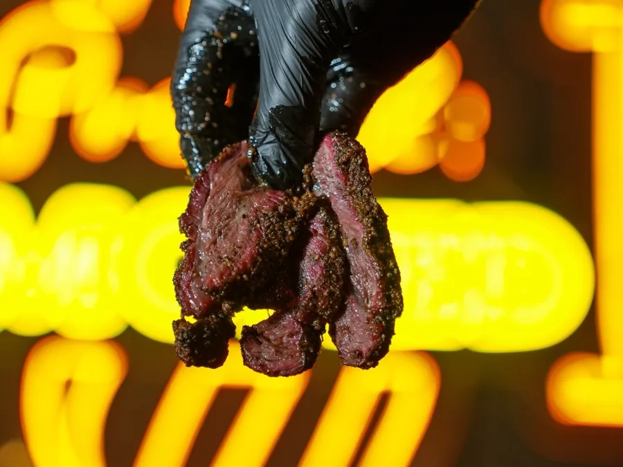 A slab of slow-smoked Angus beef cheek held up against the neon sign