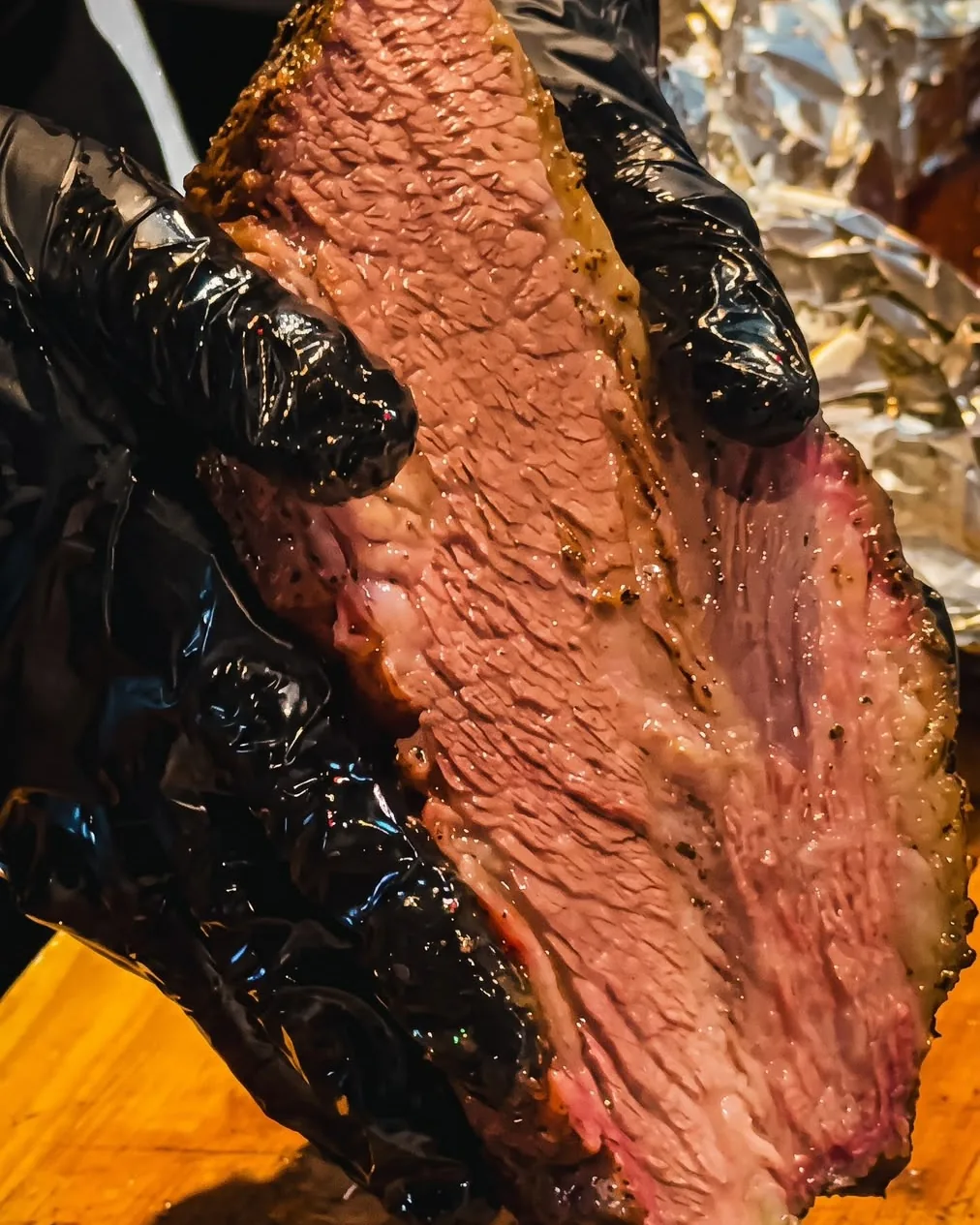 Hand holding a thick slice of smoked Angus brisket, pink smoke ring and peppery bark